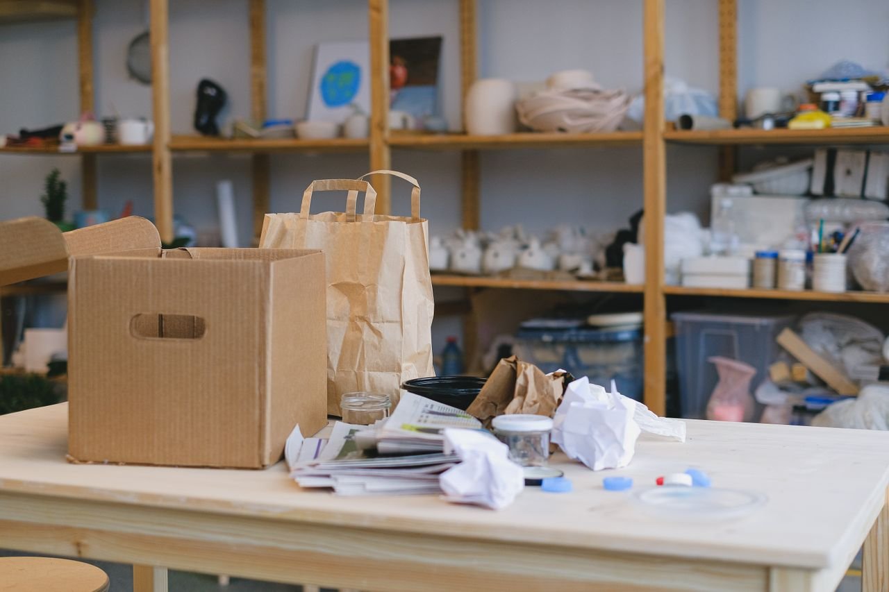 Services Cardboard box and paper bags on table in cluttered workspace with shelves. Ideal for packaging concepts.
