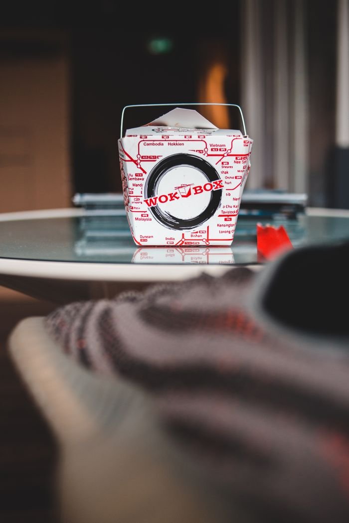 Small carton box with delicious wok food placed on small round glass table in light room